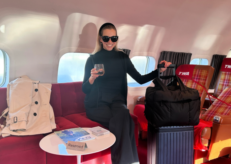 Airport Outfits: Effortlessly Stylish & Comfortable Travel Looks ALLY ON THE PLANE BAR AT TWA HOTEL AT JFK TERMINAL 5 WITH THE CARL FRIEDRICK THE CORE CARRY ON AND THE CALPAK LUKA DUFFEL STUDS EARRINGS HARLOW SUNGLASSES UNBOUND MERINO HOODIE LULULEMON PANTS