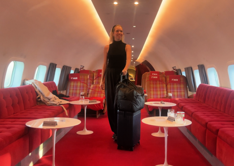 Carl Friedrik The Core Carry-On Review: Is It an Elite Bag? Ally traveling with the Carl Friedrick The Core Carry On inside the connie plane at the vintage TWA hotel at JFK Airport wearing lululemon trousers with calpak luka duffel