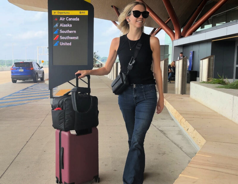 Quince Carry-On Review 2026: Worth It After 4 Real Trips? Ally at Pittsburgh Airport with the Quince carry-on and the Calpak Luka Duffel with the Bandolier Miller Crossbody, lucky jeans, and wool black tank