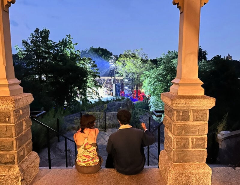 Shakespeare in the Park NYC: Your 2026 Guide to Free Theater two people watching shakespeare in the park from belvedere castle
